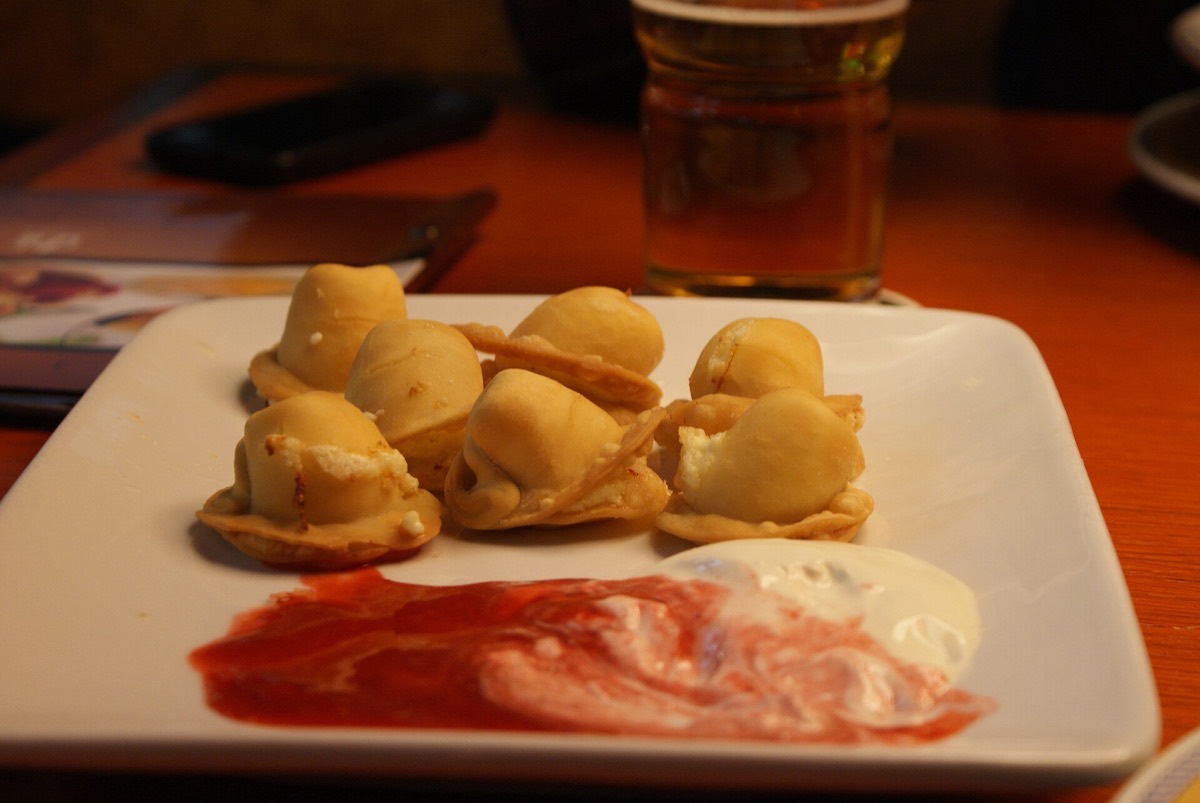 A plate of kalduny dumplings with sour cream and berry sauce